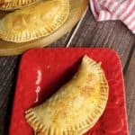 baked beef and cheese empanada on a plate with 3 more on a wood board